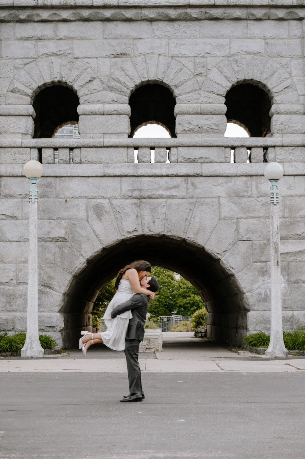 A romantic moment captured under a stone archway with decorative architectural details and white pillars.
