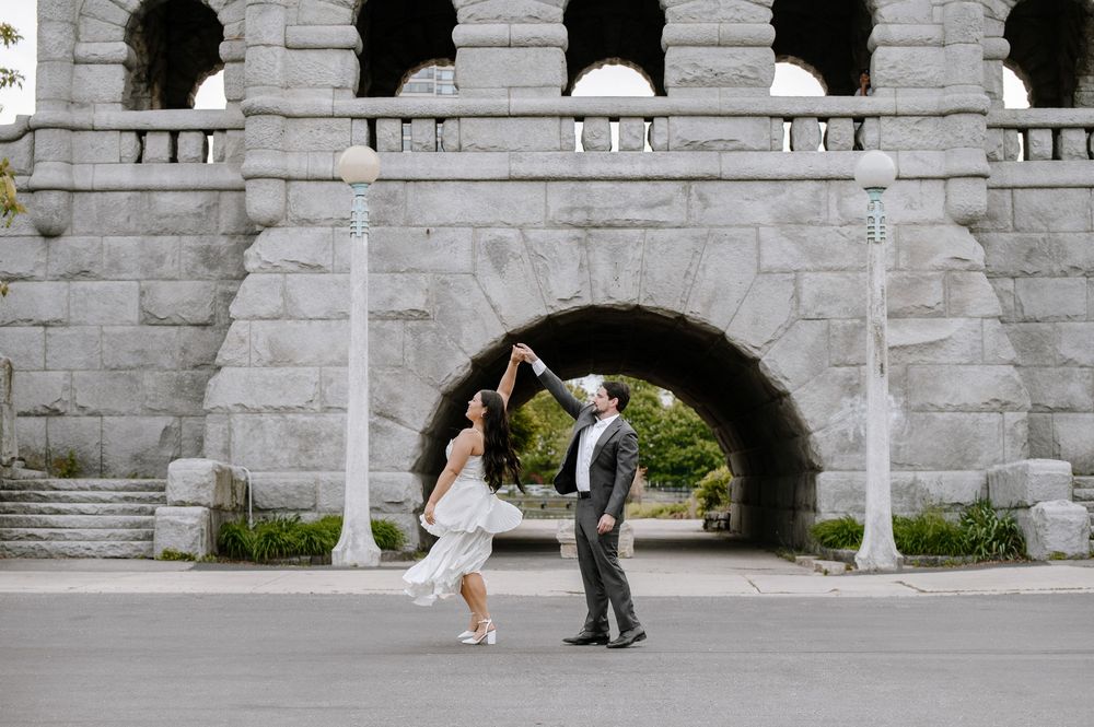 A dancing couple poses beneath a stone archway in front of lush greenery, creating an elegant portrait moment.