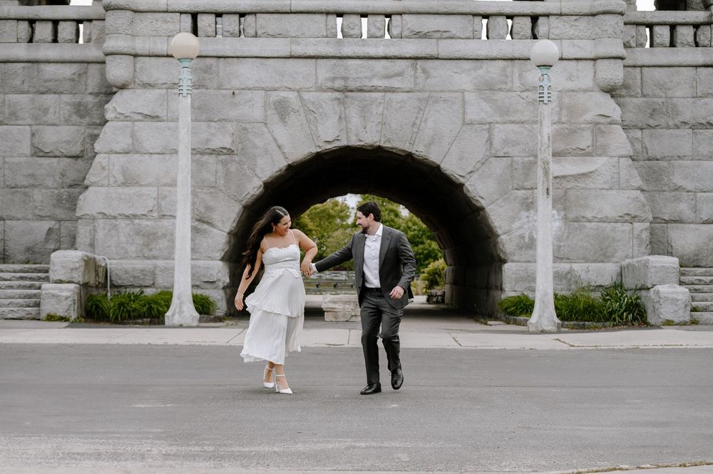 A couple dances playfully under a stone archway bridge in an urban setting.