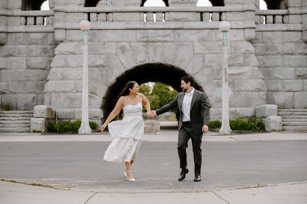 A couple in wedding attire dances playfully across a stone courtyard on their special day.