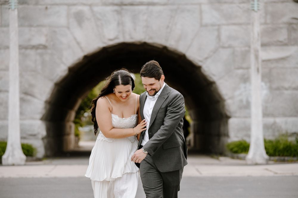 Newlywed couple walking under a stone archway and laughing together after their wedding ceremony.