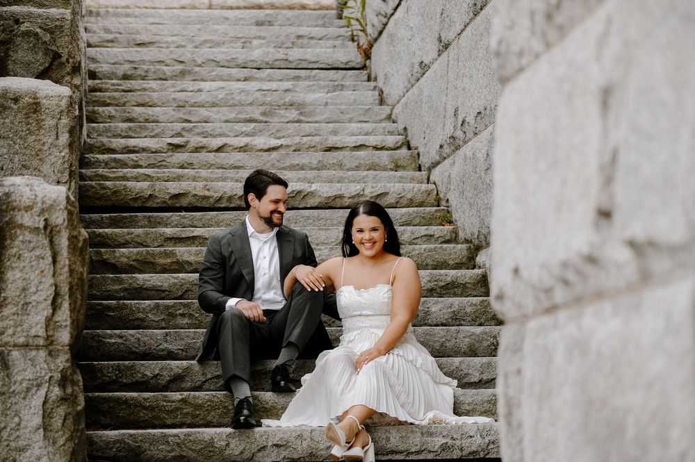 A couple in formal wedding attire sits together on stone stairs during an outdoor photo session.