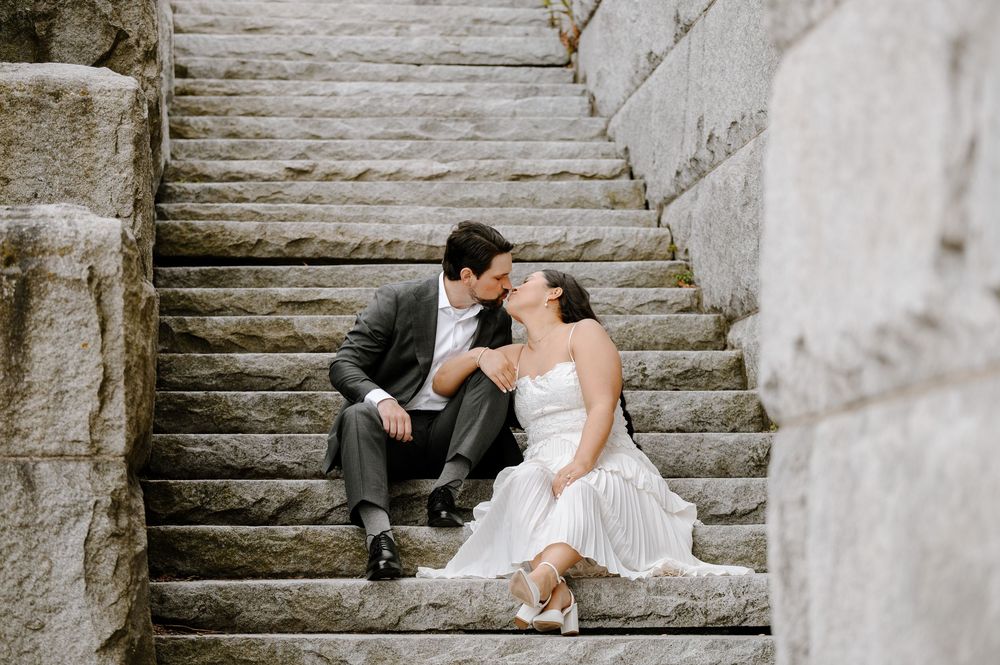 A couple in formal wedding attire sitting intimately on stone steps for a romantic outdoor portrait.