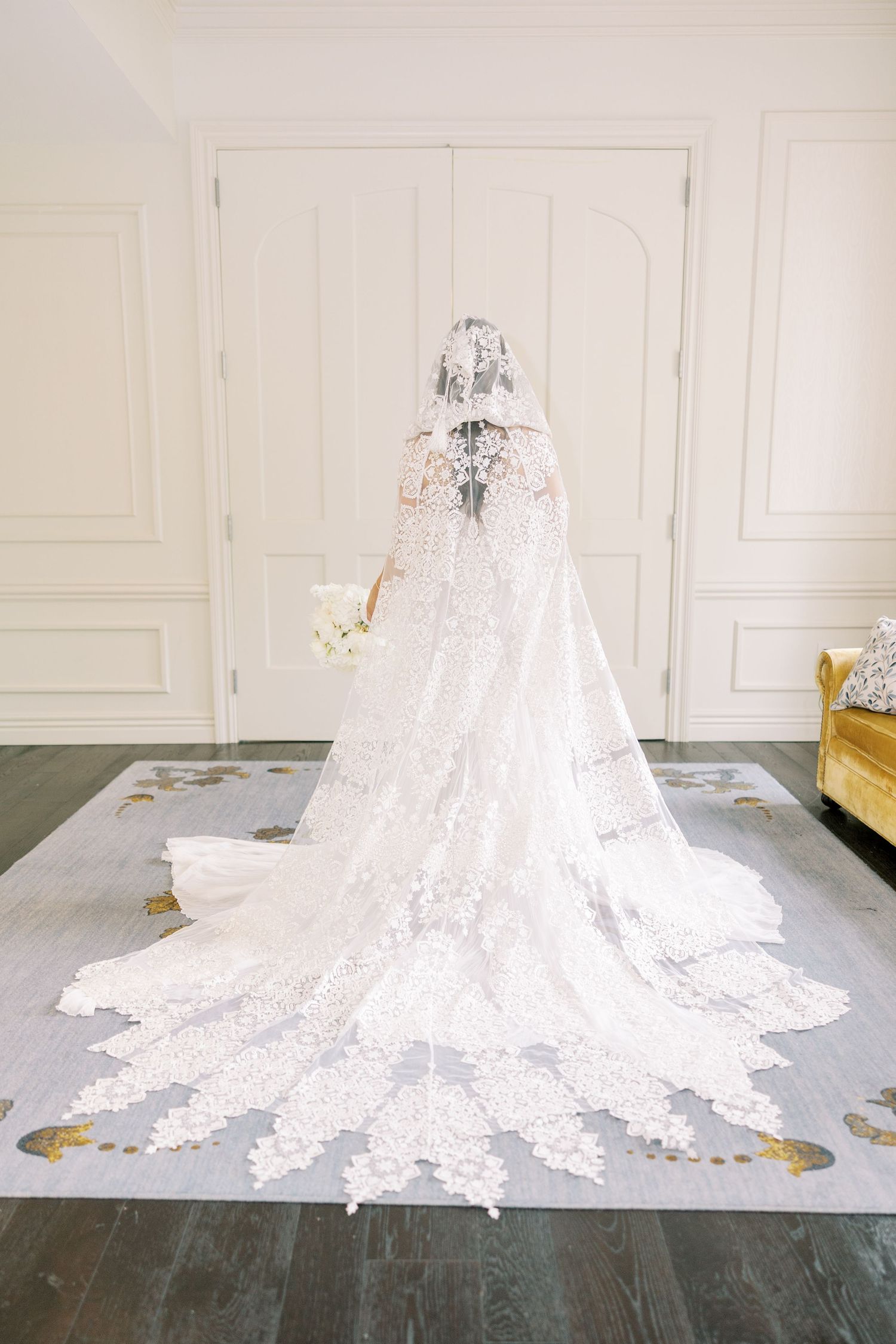 A stunning white lace wedding dress train with intricate details spreads across a dark floor in the Library Suite at The Adelphi Hotel.