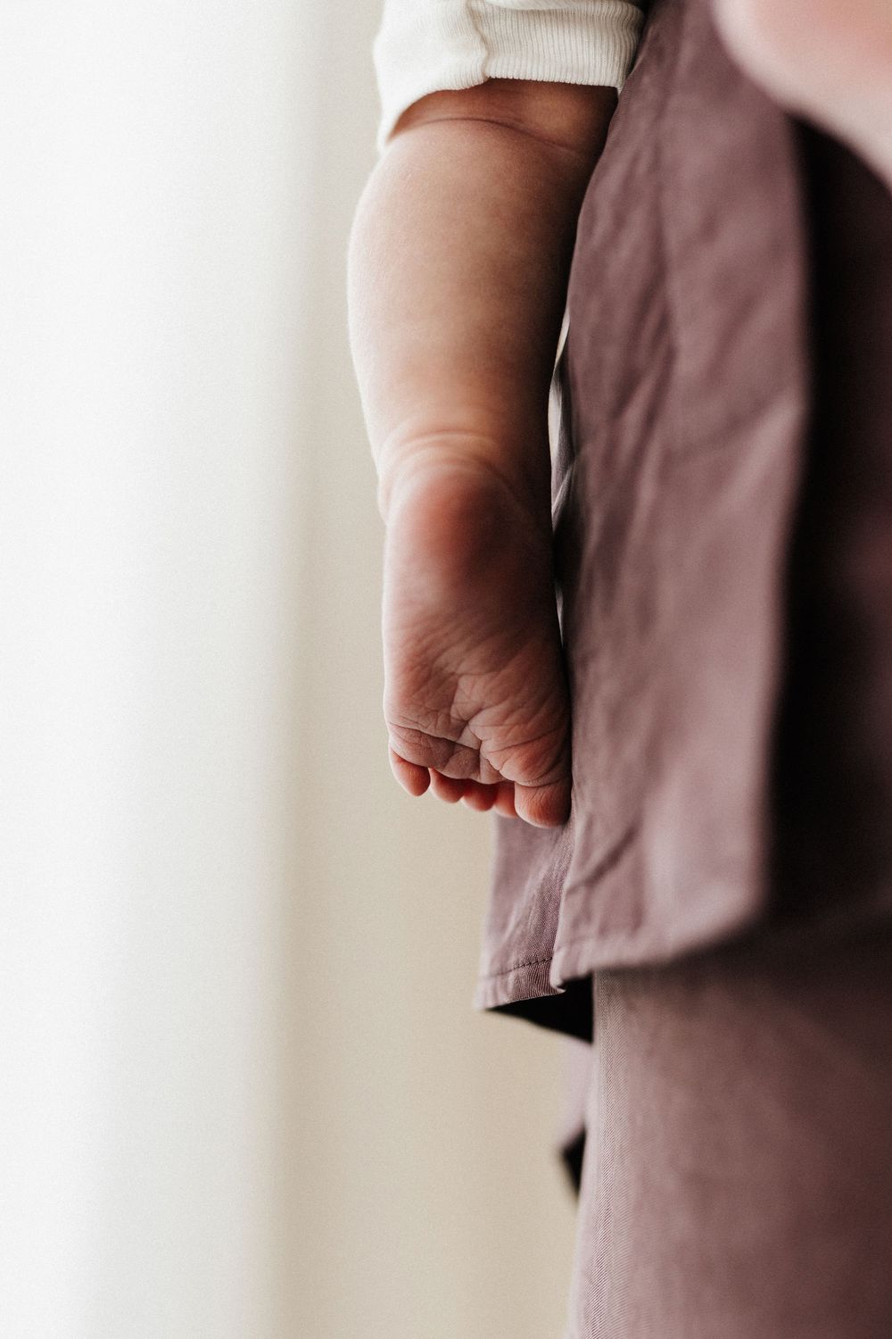 Close-up view of a baby's tiny foot and leg against mauve colored clothing in soft natural lighting.