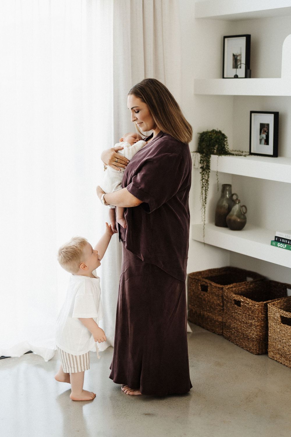 A series of four tender moments between parent and child in a bright white minimalist room with woven baskets.