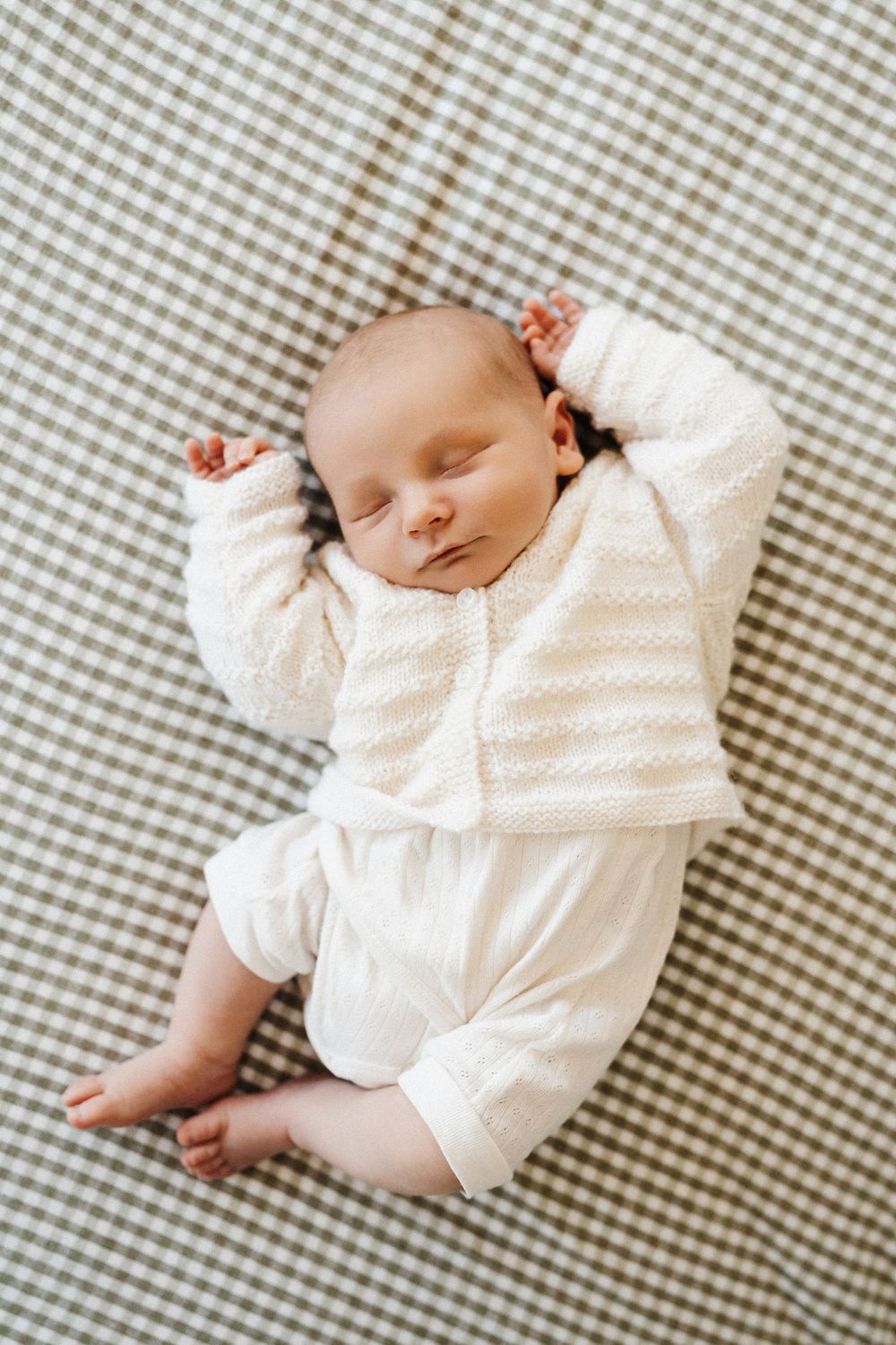 A baby lying on a bed wearing a cozy cream outfit.