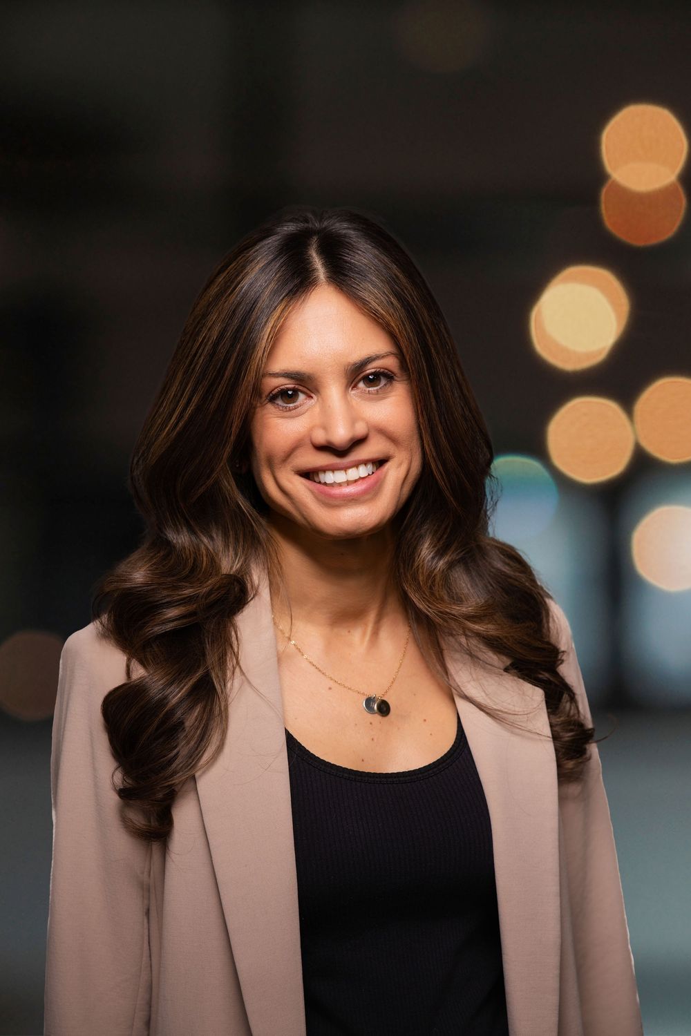 Professional therapist wearing a tan blazer and black top with soft lighting and bokeh background in headshot series.