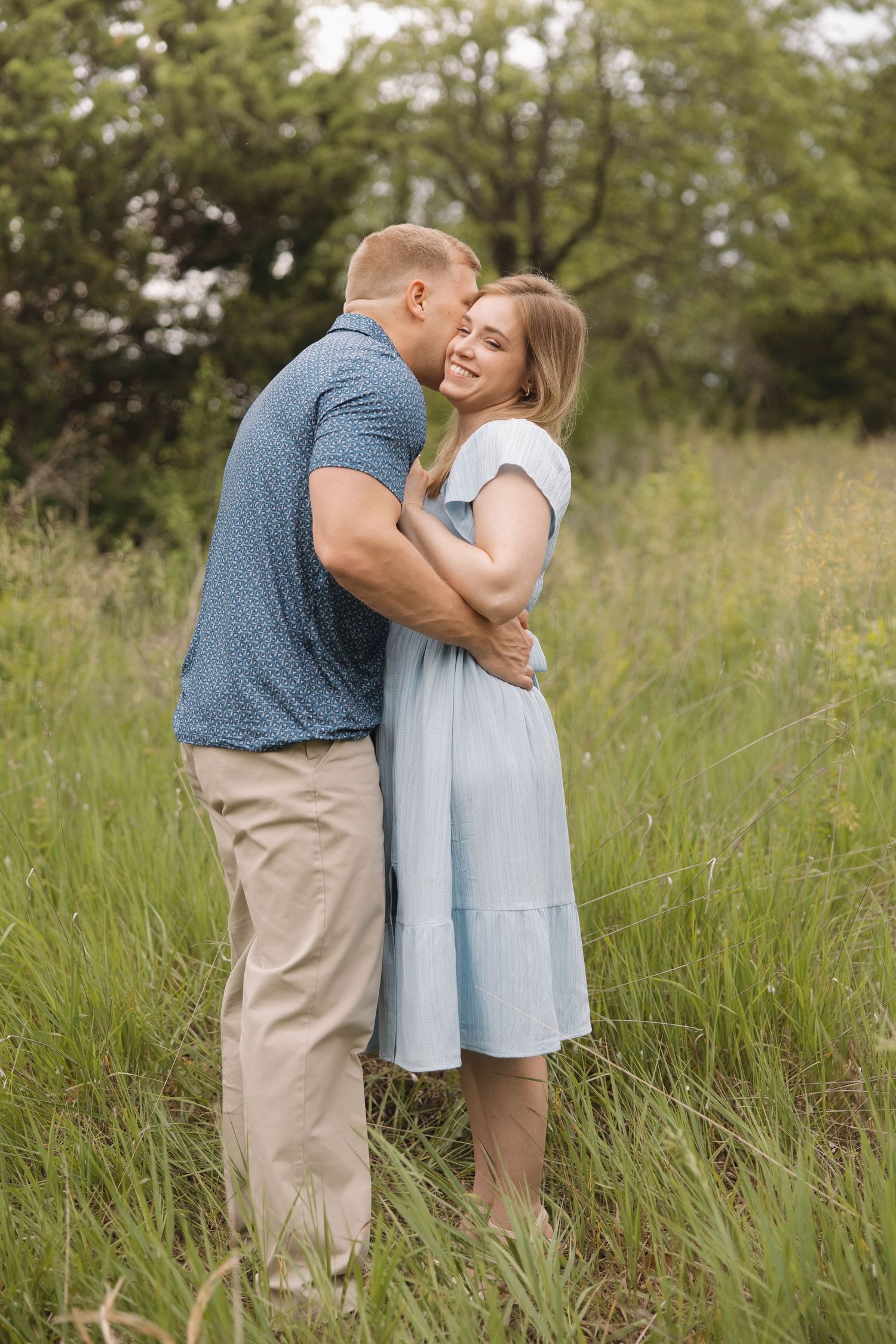 A couple embraces in a sunny meadow during a romantic photoshoot in soft sunlight and tall grass.