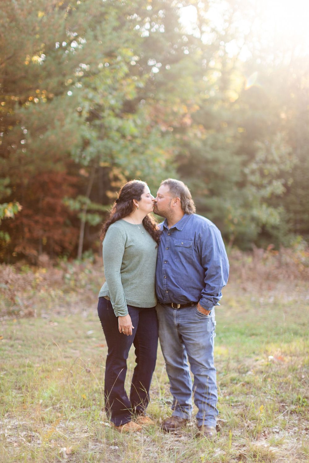 A romantic sunset photo of a couple sharing a tender moment together in a wooded clearing.