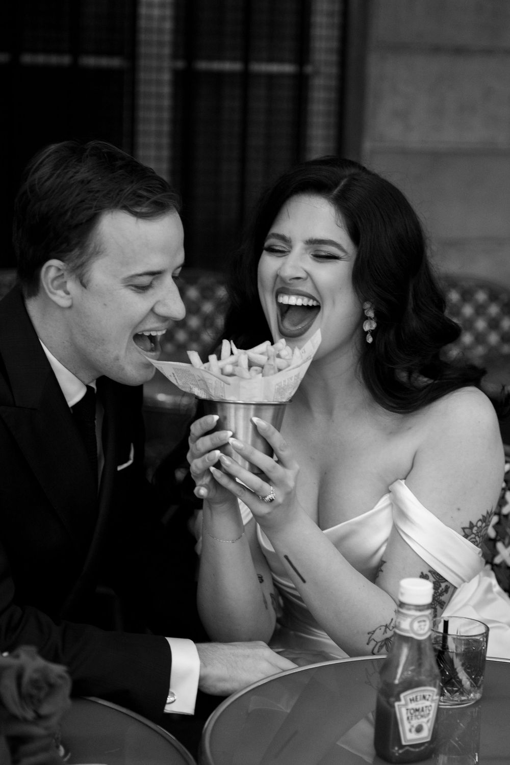 Black and white photo of a couple sharing dessert and laughing during their wedding reception.