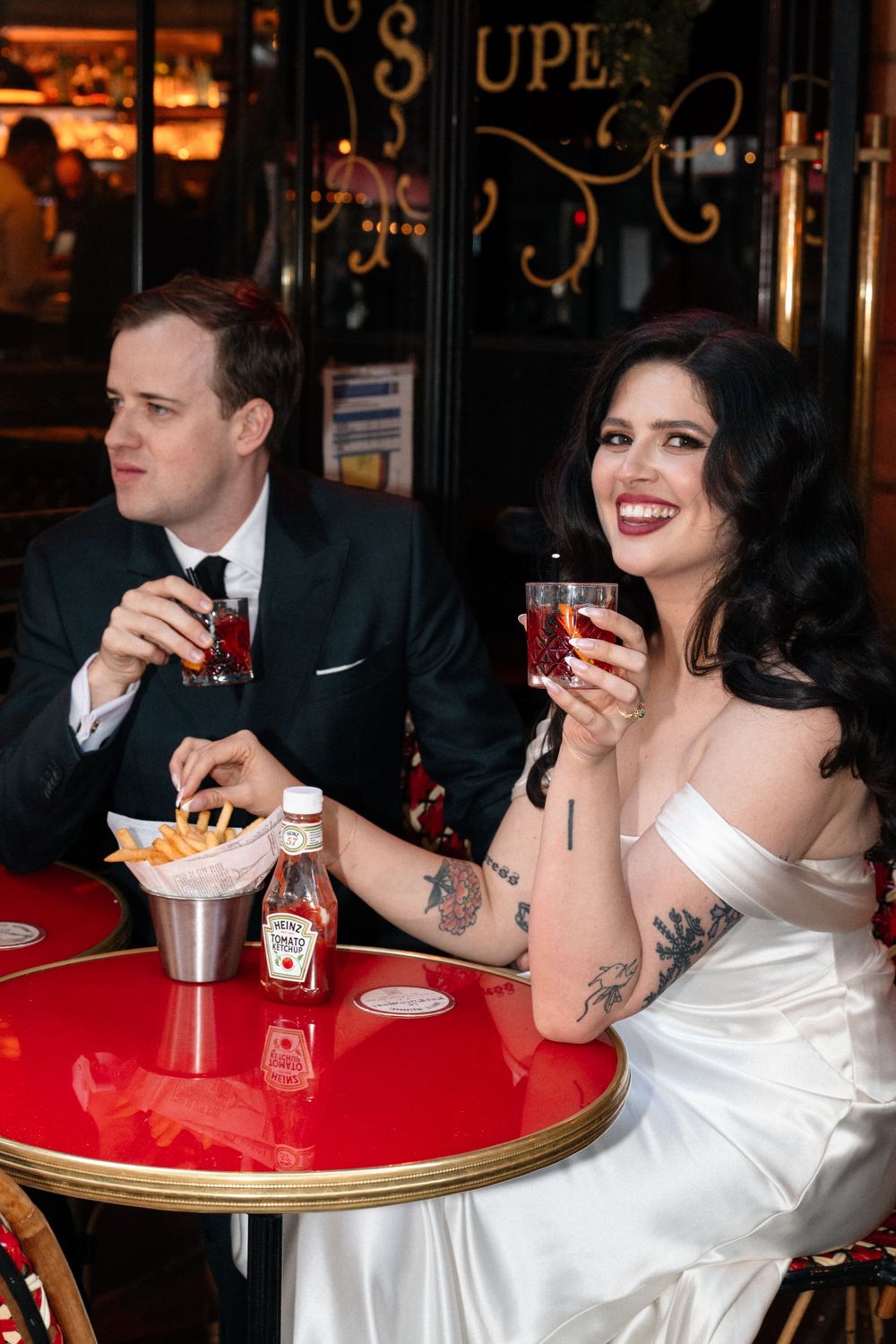 Couple enjoying drinks at a red bistro table in vintage-style setting.