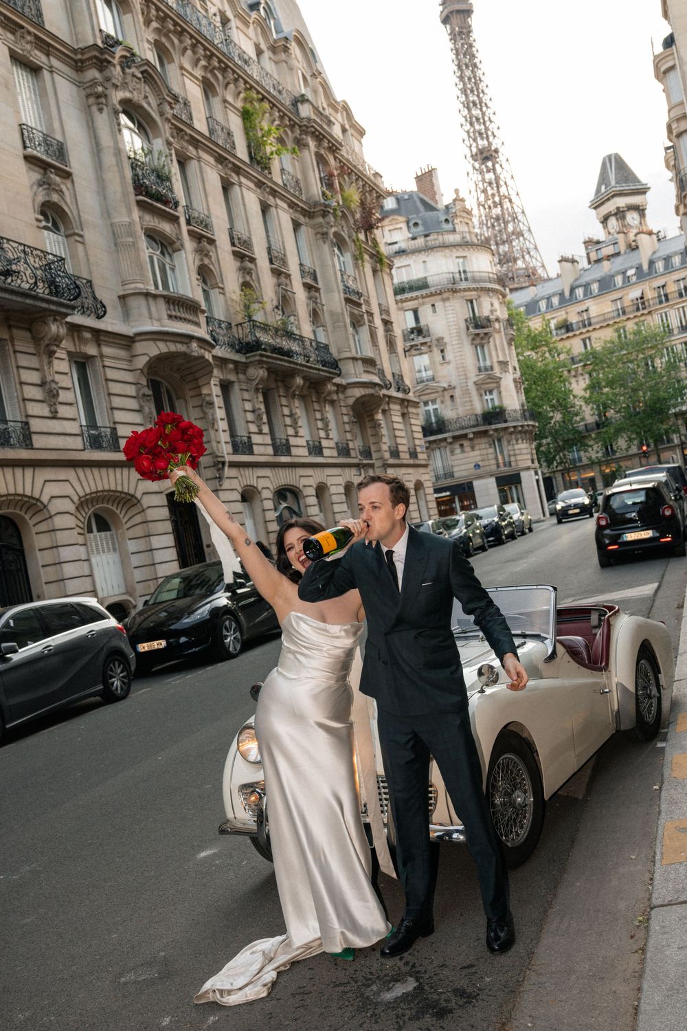 Couple in wedding attire posing on a charming Parisian street with classic architecture in the background.