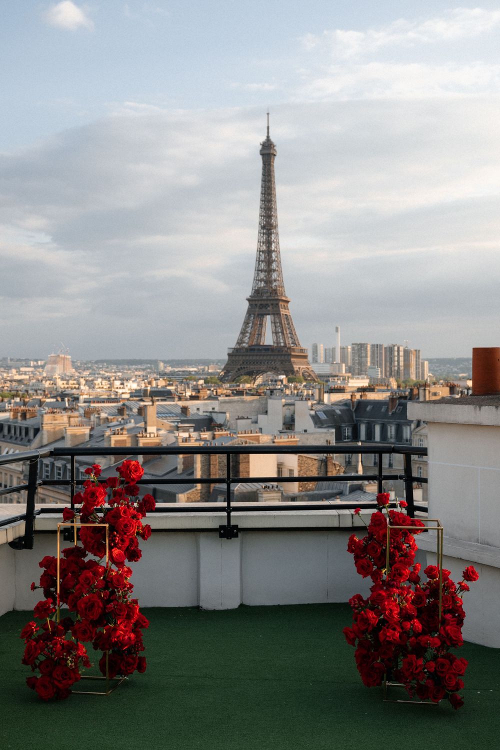 A romantic rooftop terrace in Paris with red roses and the iconic Eiffel Tower visible against a cloudy sky.