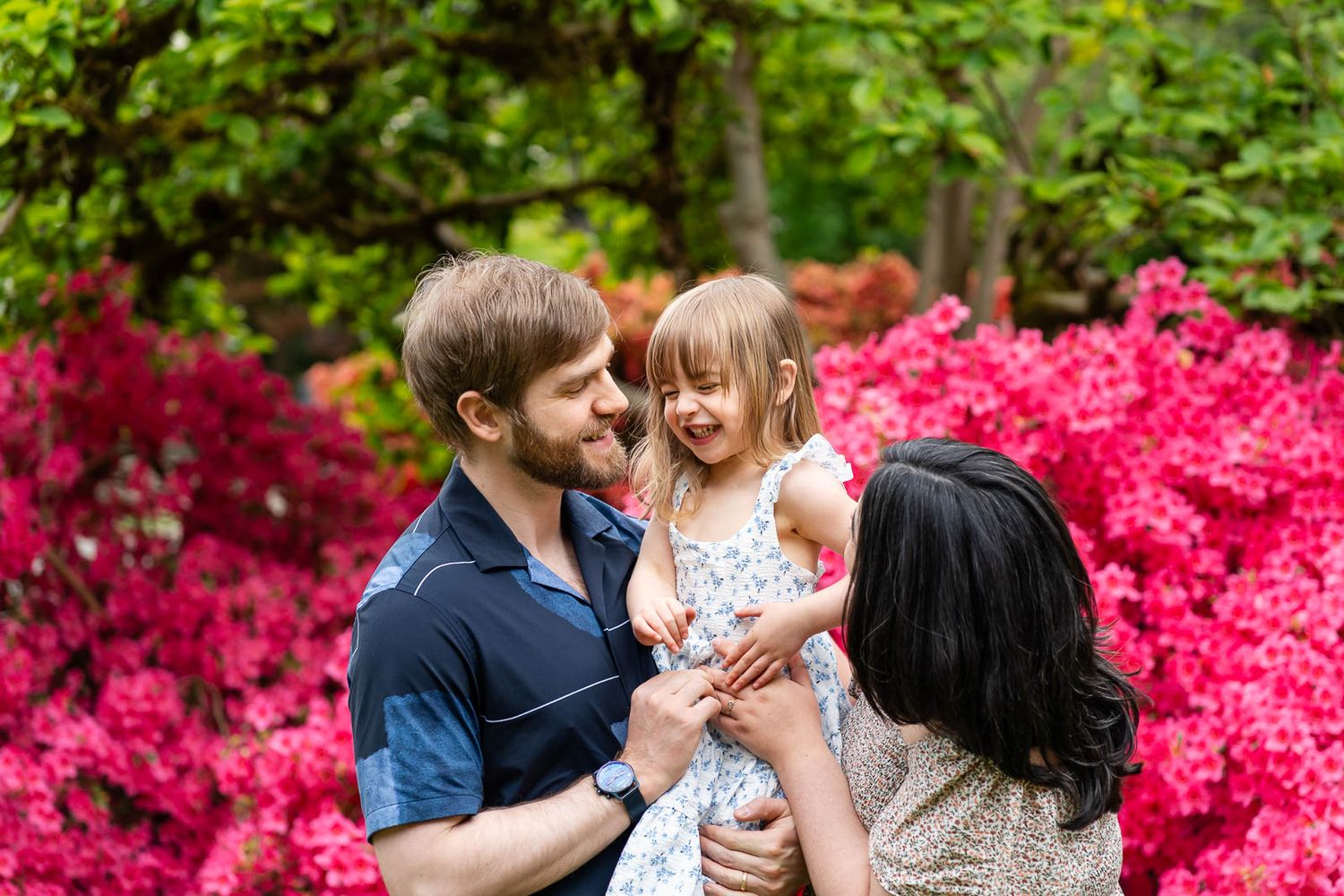 Family tickles daughter in front of the azaleas.