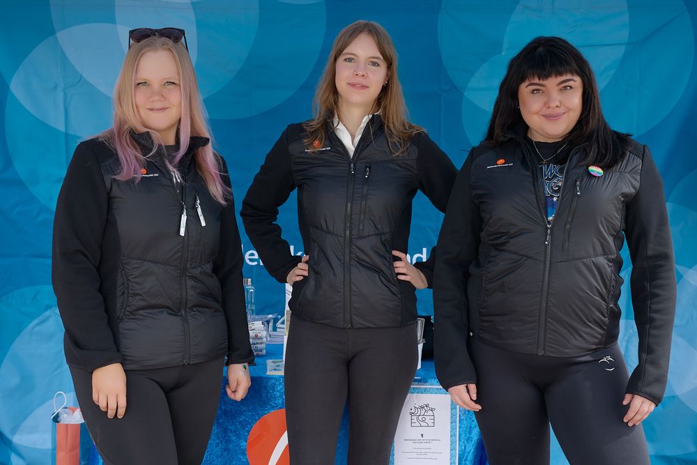 Three women in winter athletic wear stand together in front of a blue backdrop with their hands on their hips.