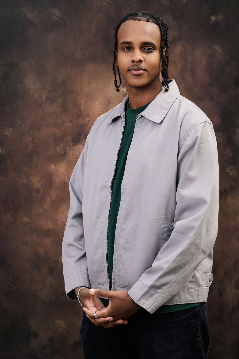 Professional studio portrait of someone wearing a white collared shirt with dark green top against a textured brown backdrop.