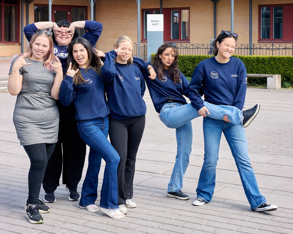 Group in matching navy blue sweatshirts strike fun poses together outdoors on a sunny day.