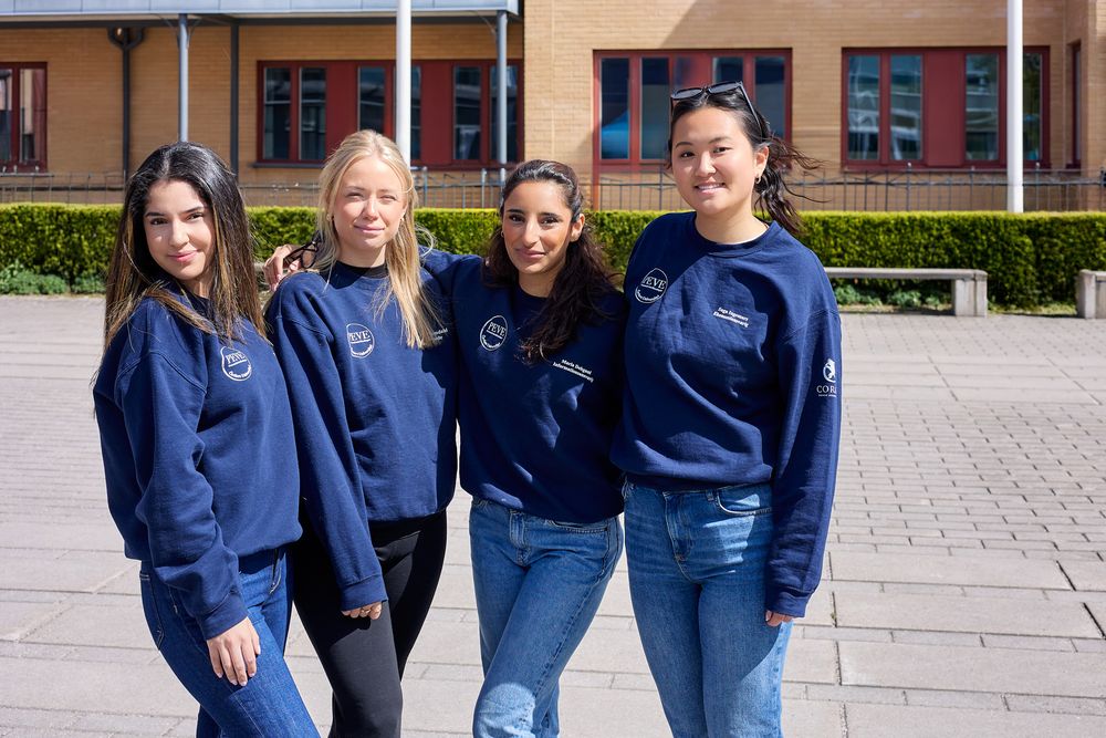 Group wearing matching navy blue uniforms stands together on paved walkway outside brick building.