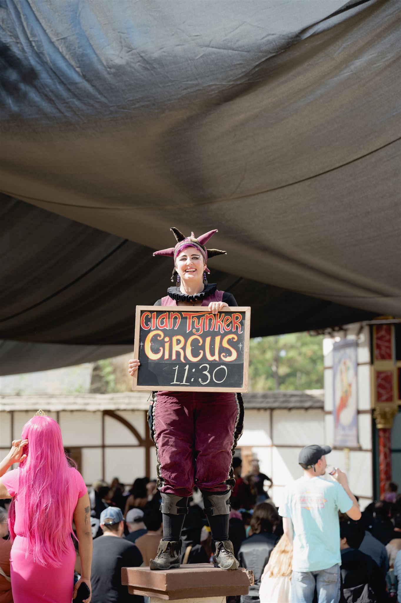 A progressive sequence of pink-haired carnival performer signs being hung up at a circus event under a tent canopy.