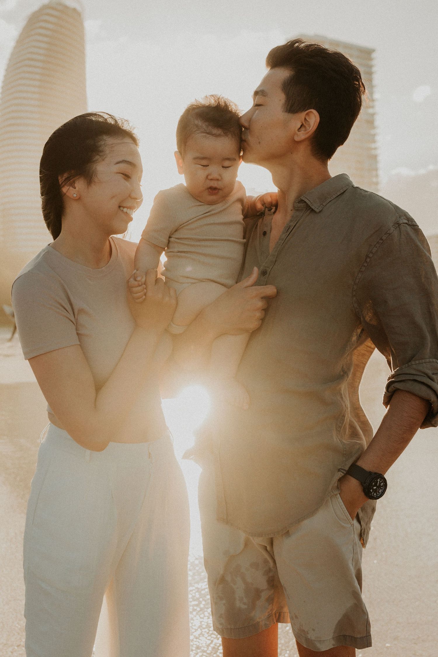 A family lying together on white bedding with toddler in middle and pregnant person showing baby bump.