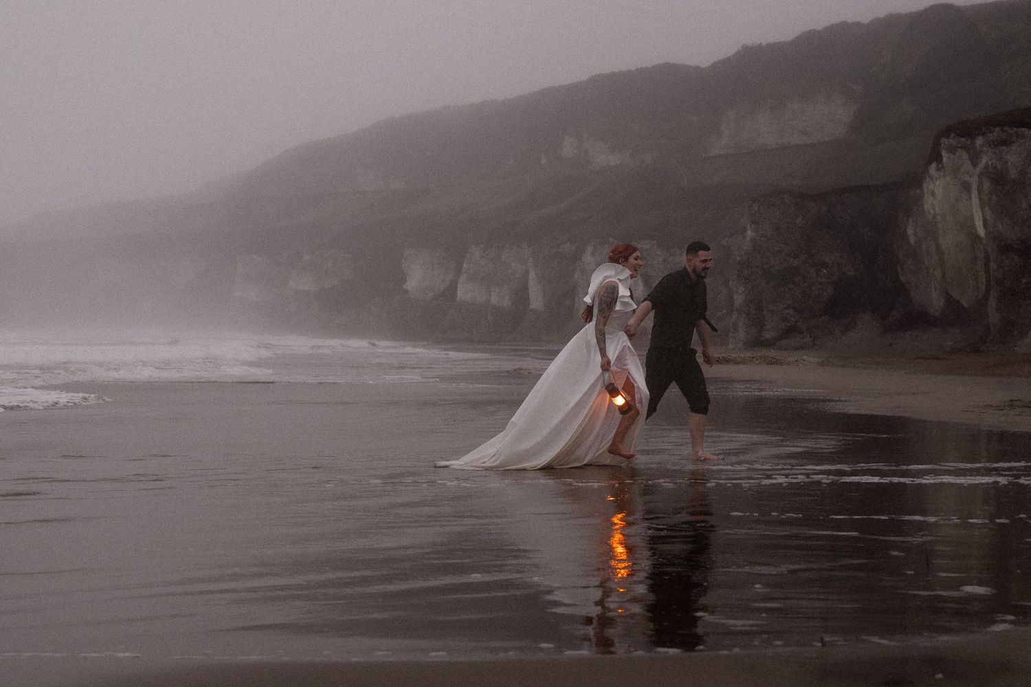Natural elopement photography of bride and groom in nature along a misty beach with rugged cliffs and a lantern reflection isand.