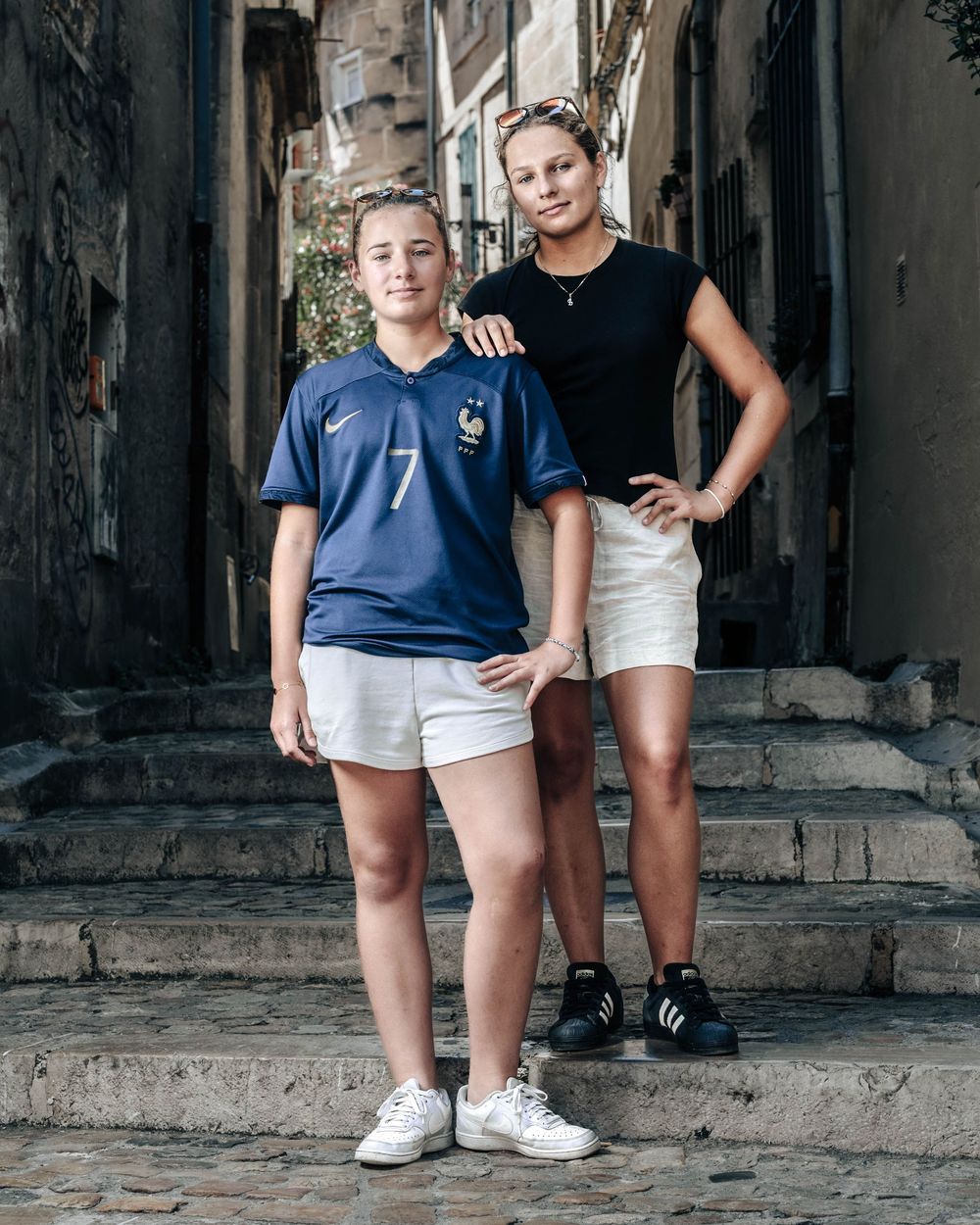 Two people stand together posing on worn stone steps in an old narrow alleyway.