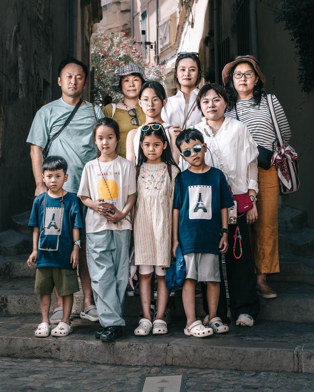 A group of children standing together against a dark wall wearing casual clothing and holding photographs.