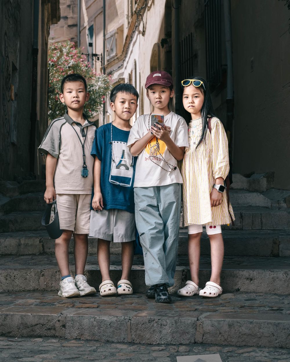 Several children stand in a line wearing casual attire against a rugged stone wall backdrop in a vintage setting.