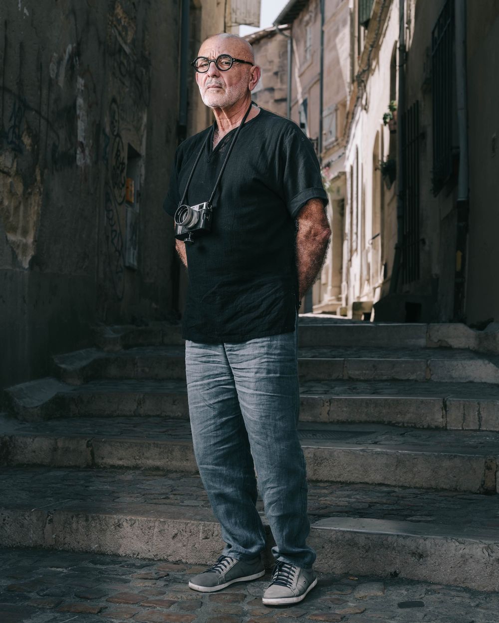 A series of five cropped photos showing someone wearing glasses, black t-shirt and jeans standing against a stone wall.