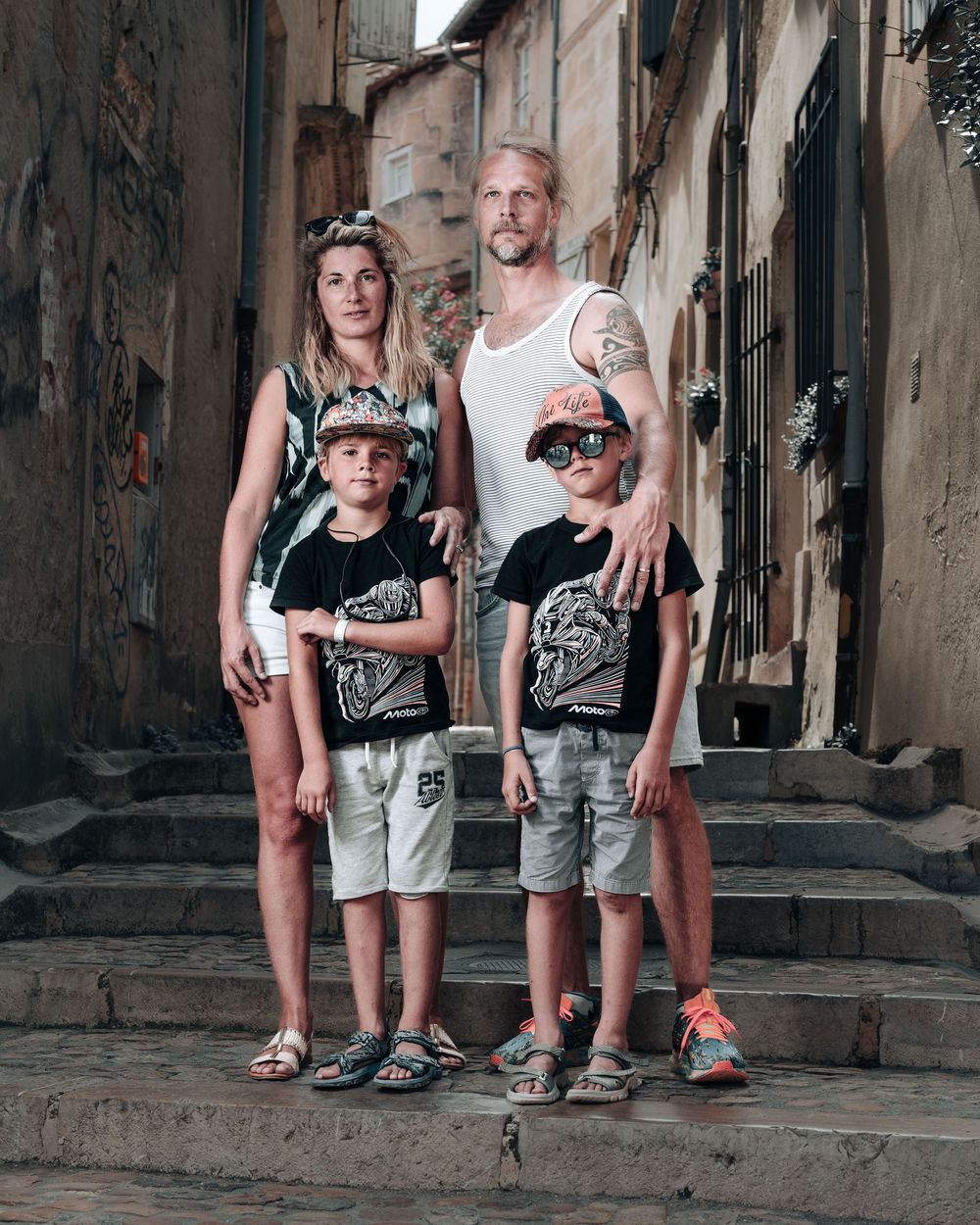 Family wearing matching black and white outfits pose together on stone steps in a narrow European alley.