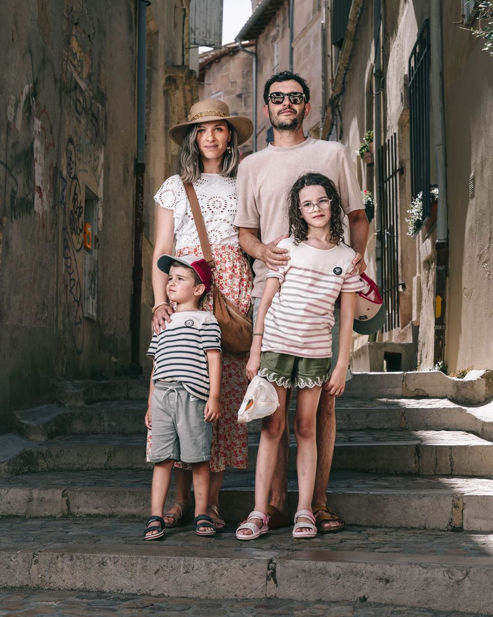 A family wearing coordinated striped outfits poses together on old stone steps in a narrow European alley.
