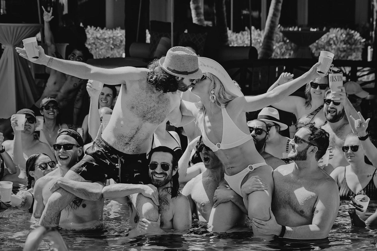 Happy couple jumps and splashes in the ocean water at a tropical beach with white clouds in black and white during their trash the dress