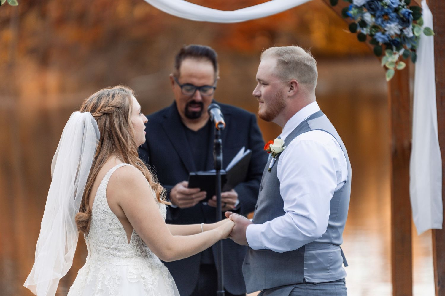 A joyous moment during an outdoor wedding ceremony under a floral arch on a sunny autumn day.