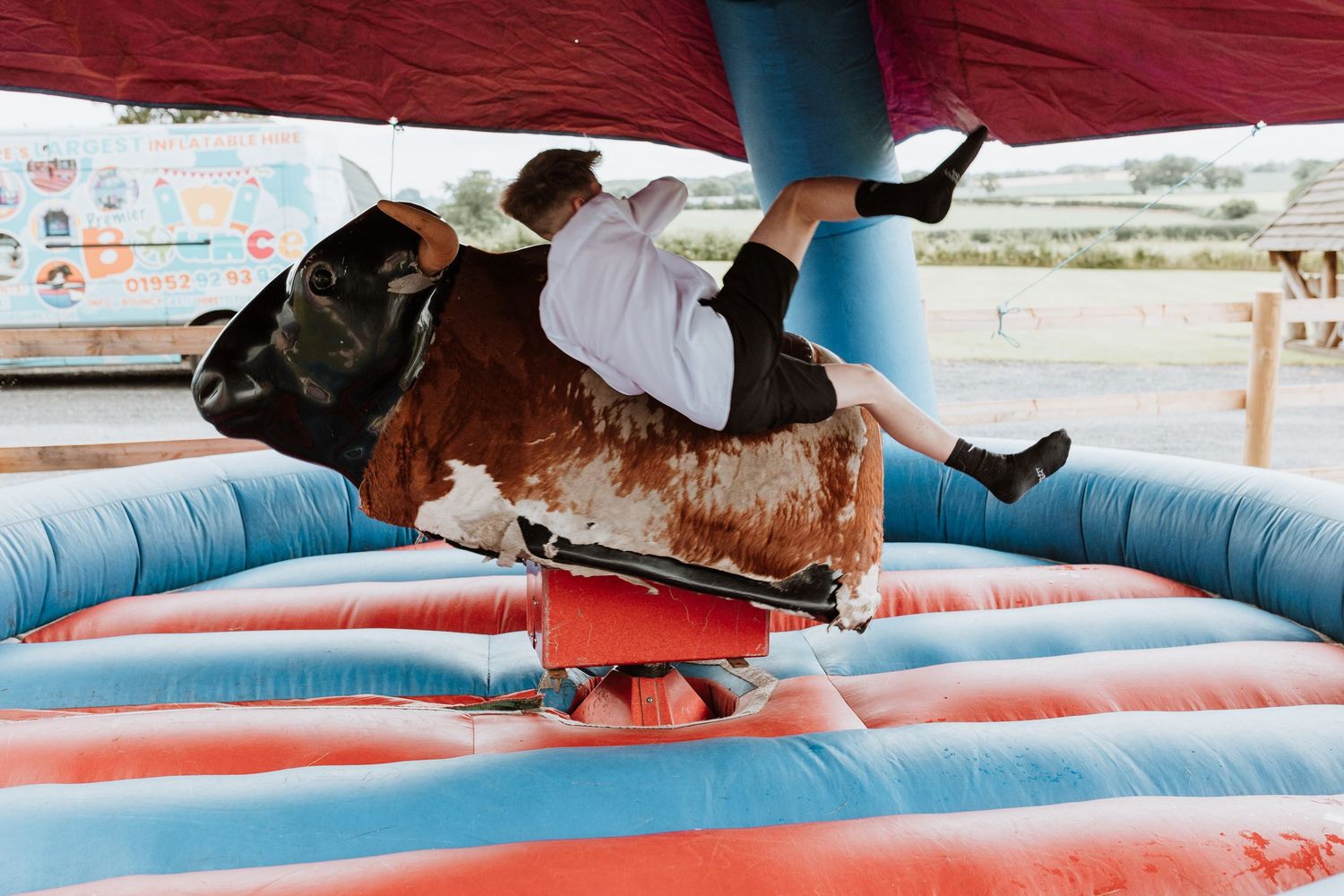 Wedding guest riding a mechanical bull at a carnival on an inflatable blue and red padded surface.
