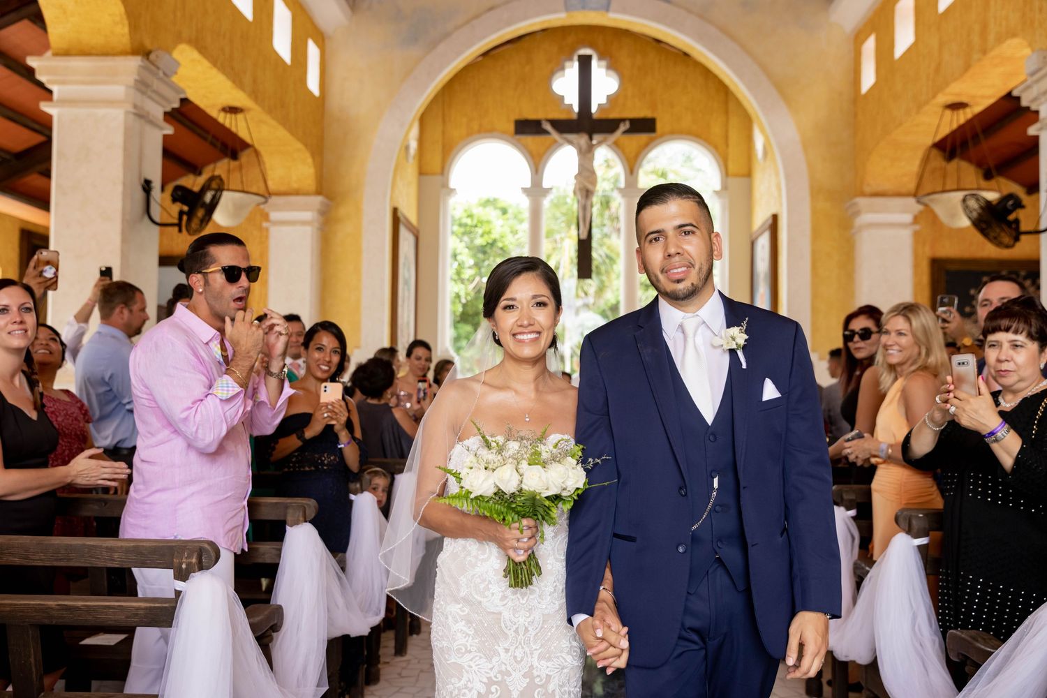 Newlyweds celebrate in church aisle as guests applaud during joyful wedding ceremony.