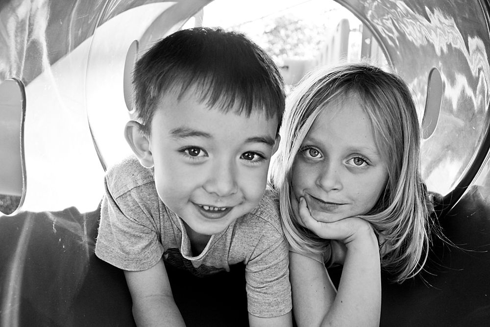 Black and white portrait of a young child and adult laying down together and smiling indoors in a relaxed pose. Family portrait.