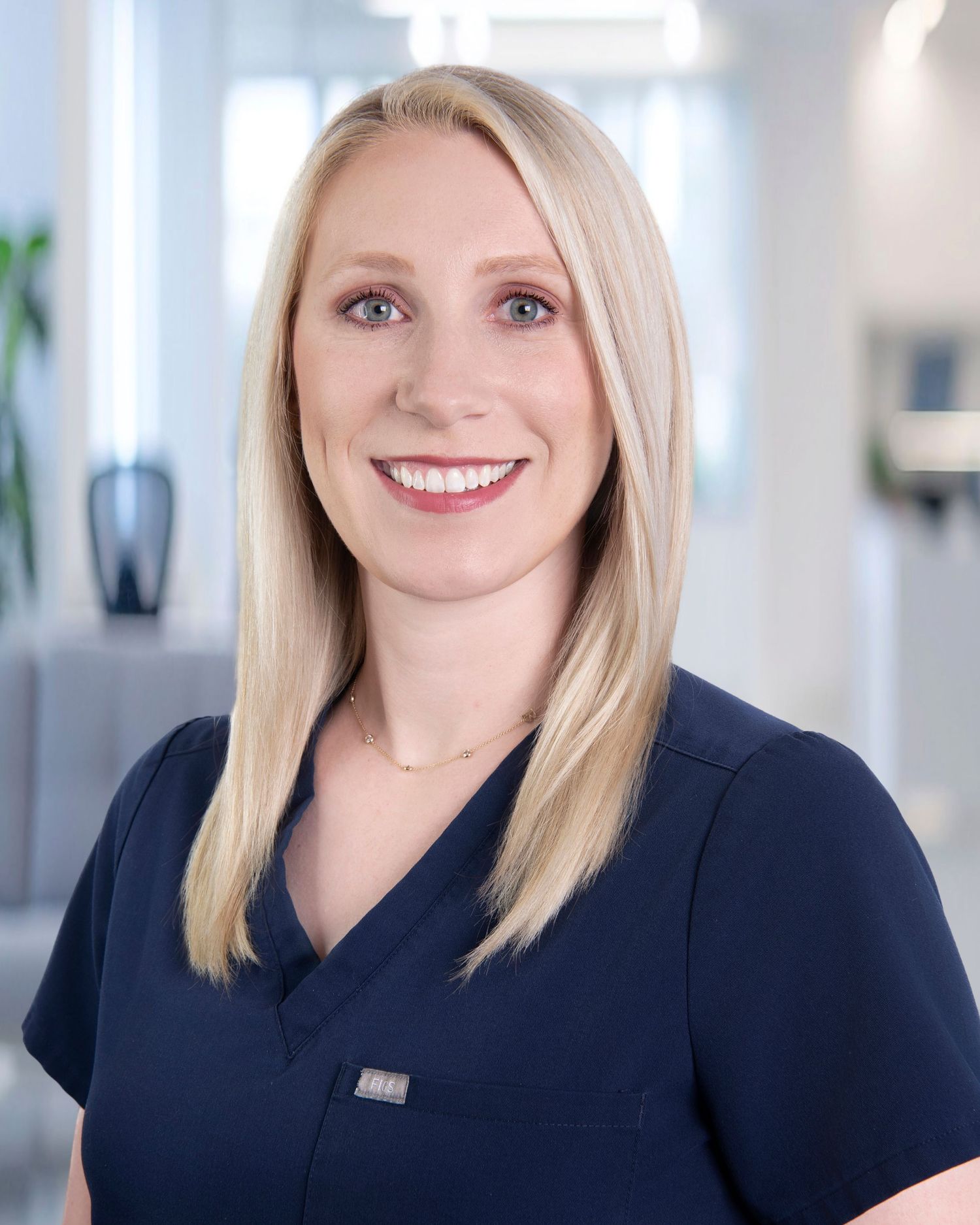 Healthcare professional in navy blue scrubs smiling warmly in a medical office setting.