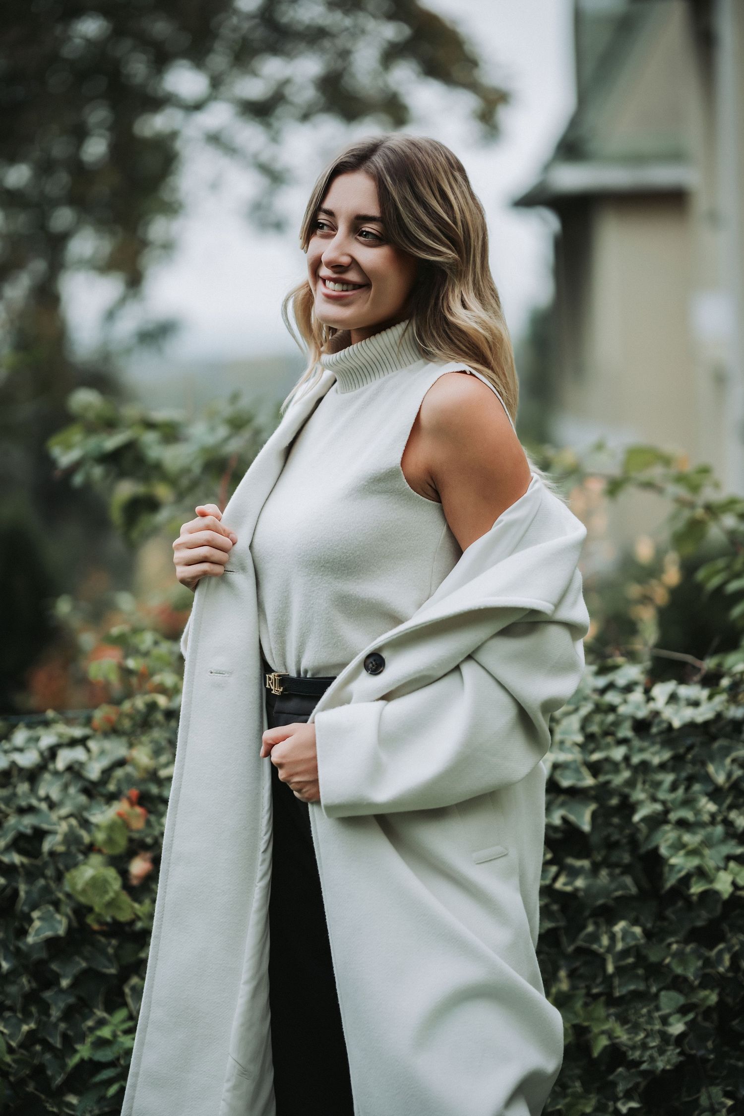 Lifestyle portrait of woman in white coat standing in garden setting.