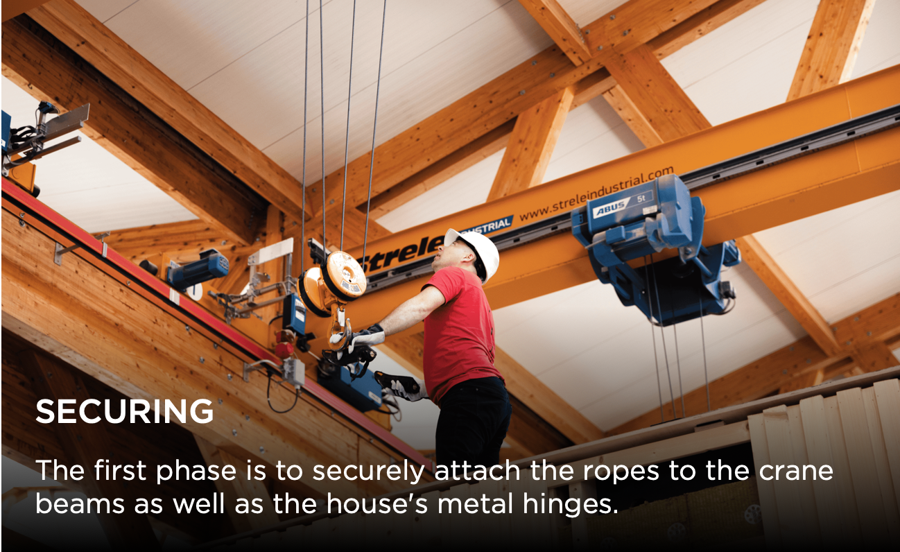 Worker in red attaches safety ropes to overhead crane beams during residential construction installation.