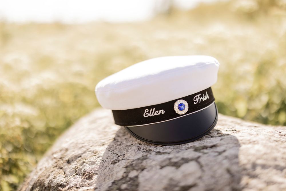 A white and black graduation cap with the name 'Ellen' sits on a gray rock in outdoor sunlight.