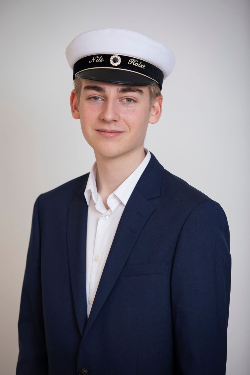 Student wearing a white sailor cap with navy blazer and white dress shirt poses for formal portrait.