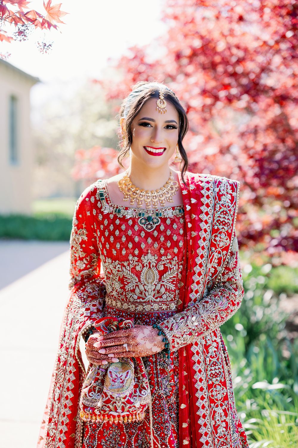 Traditional bridal attire featuring an ornate red lehenga with silver embellishments against pink floral spring blossoms.