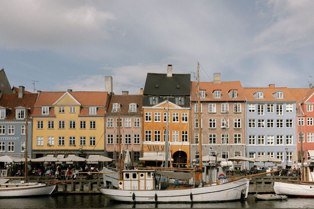 Colorful row of historic buildings along Copenhagen's Nyhavn waterfront with boats docked in the harbor. Destination wedding photographer