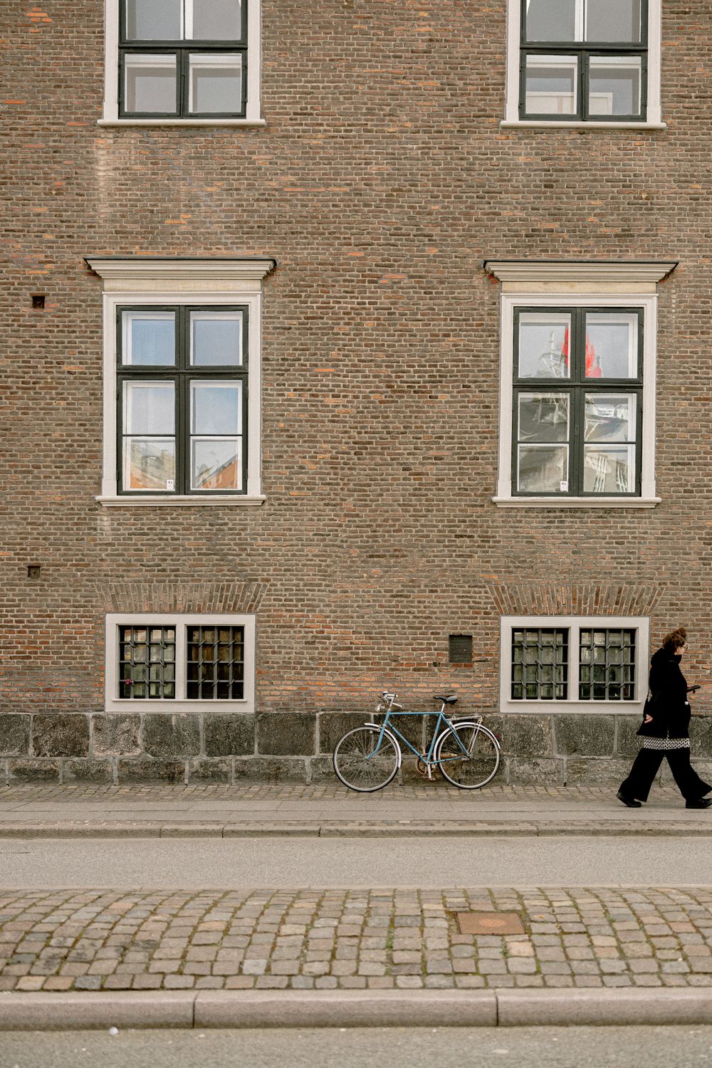 Brick building facade with symmetrical windows and a bicycle leaning against the wall.