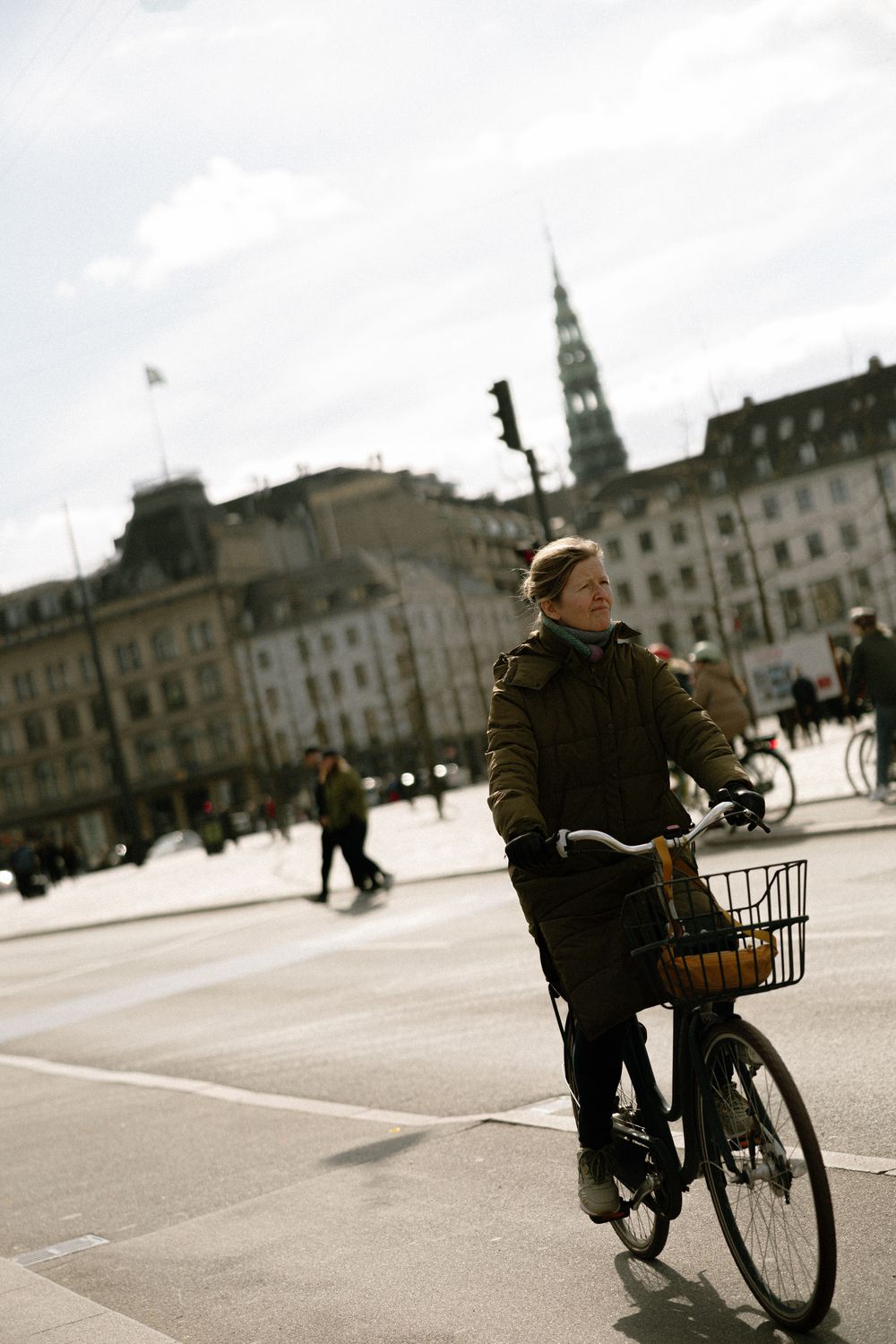 Person riding a bicycle in a winter coat against historic city architecture. Destination wedding photographer Copenhagen