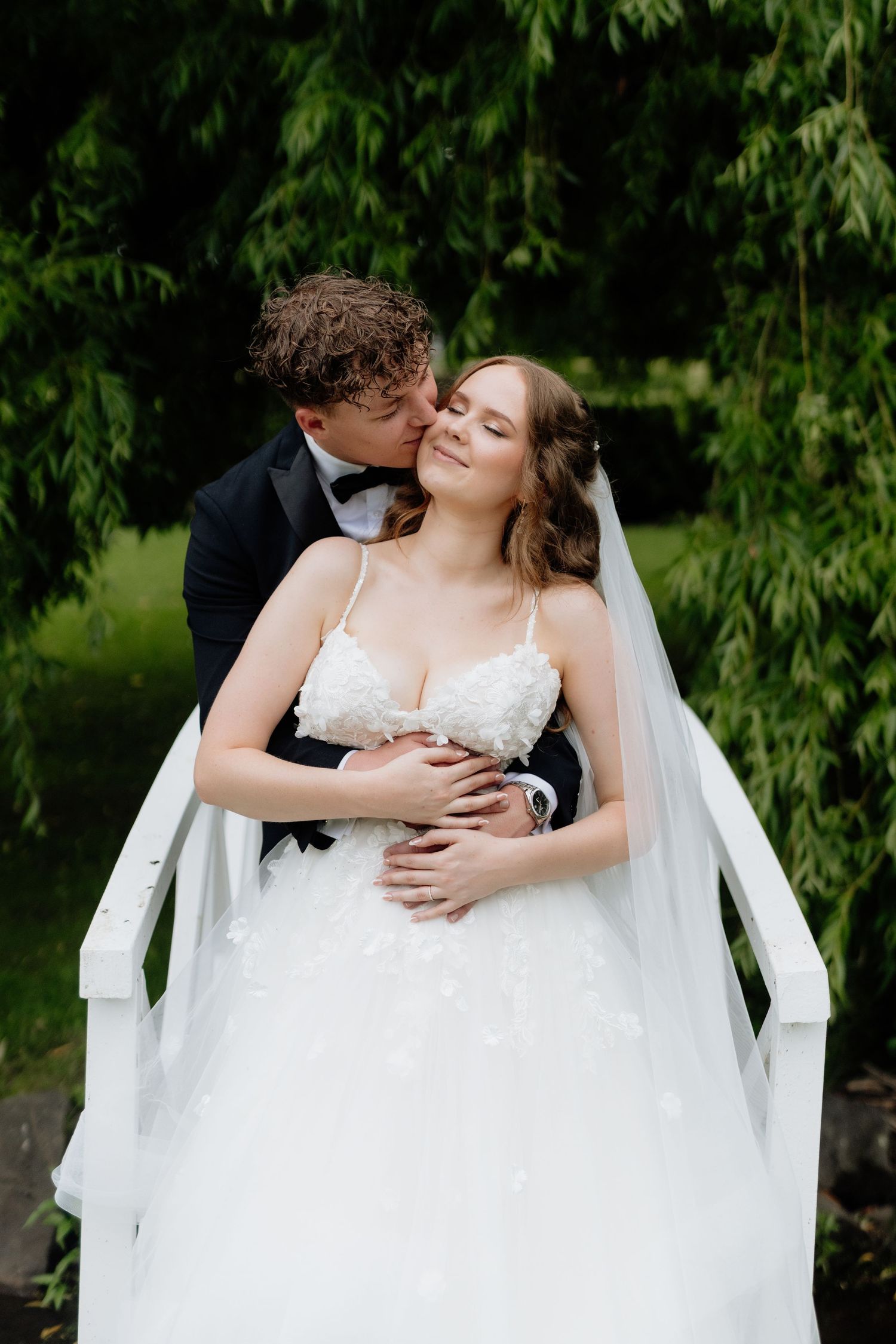 A romantic wedding moment captured outdoors with a flowing white dress and veil against lush green foliage.