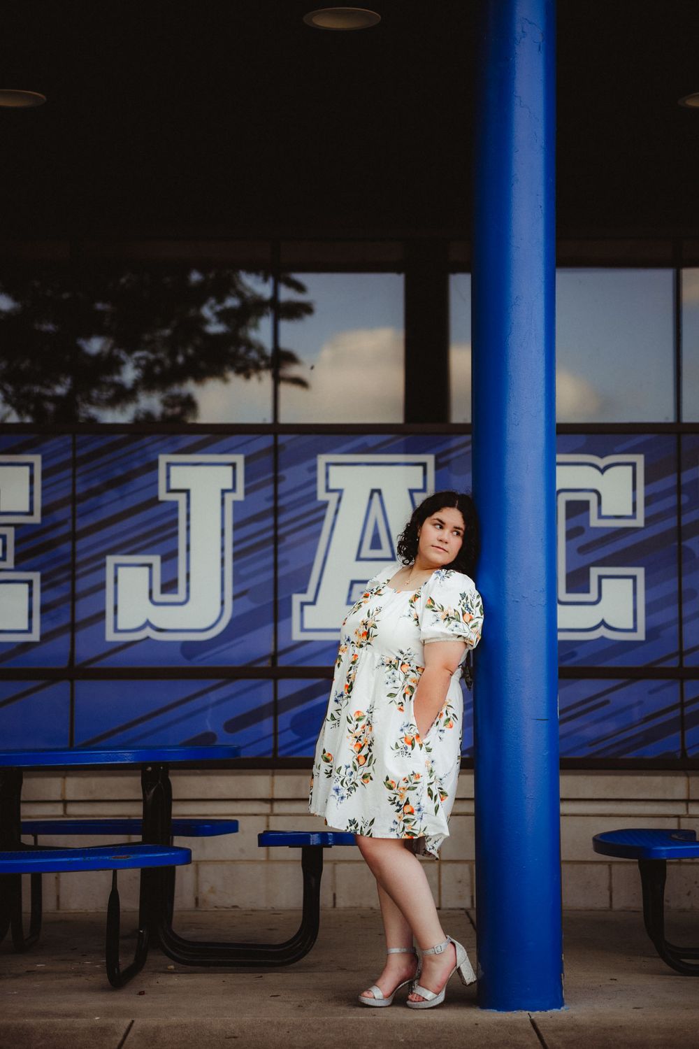 A white floral dress stands out against blue pillars and lettering in an outdoor covered seating area.