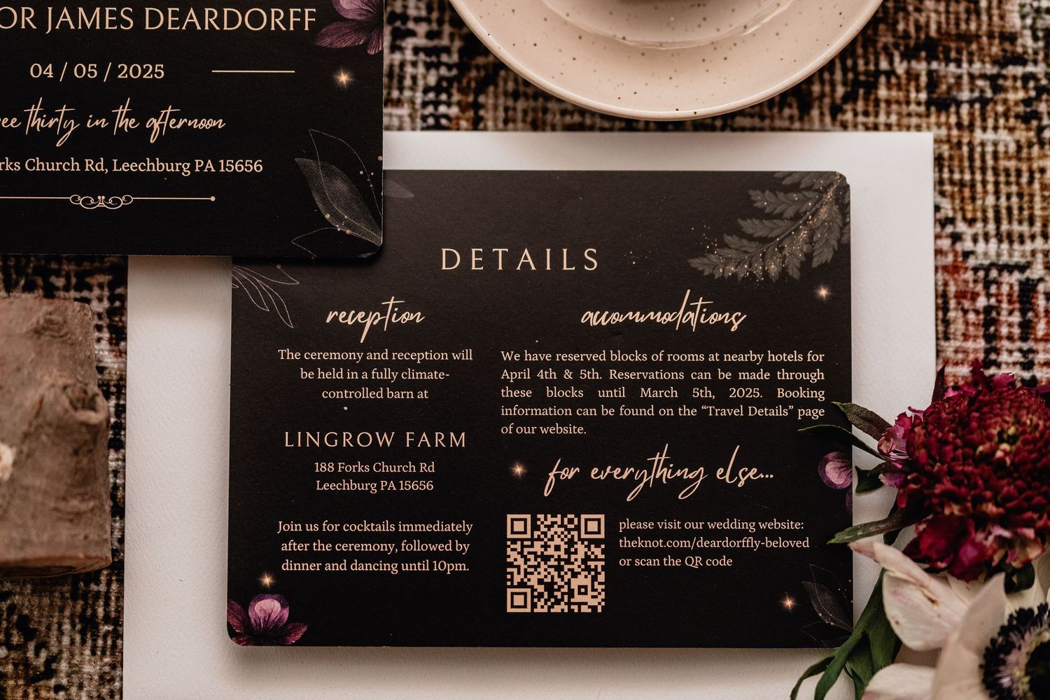 Flat lay of elegant black wedding details card with gold script, QR code, floral accents, and rustic vintage wedding decor.