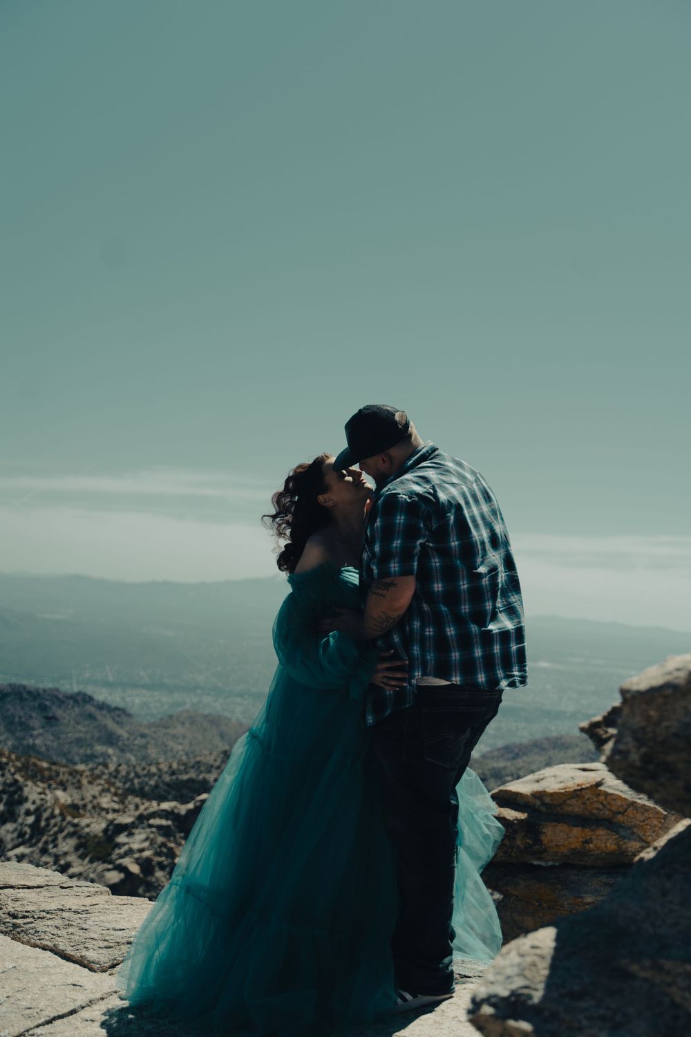 A romantic couple in formal wear share an intimate moment on a mountain overlook.